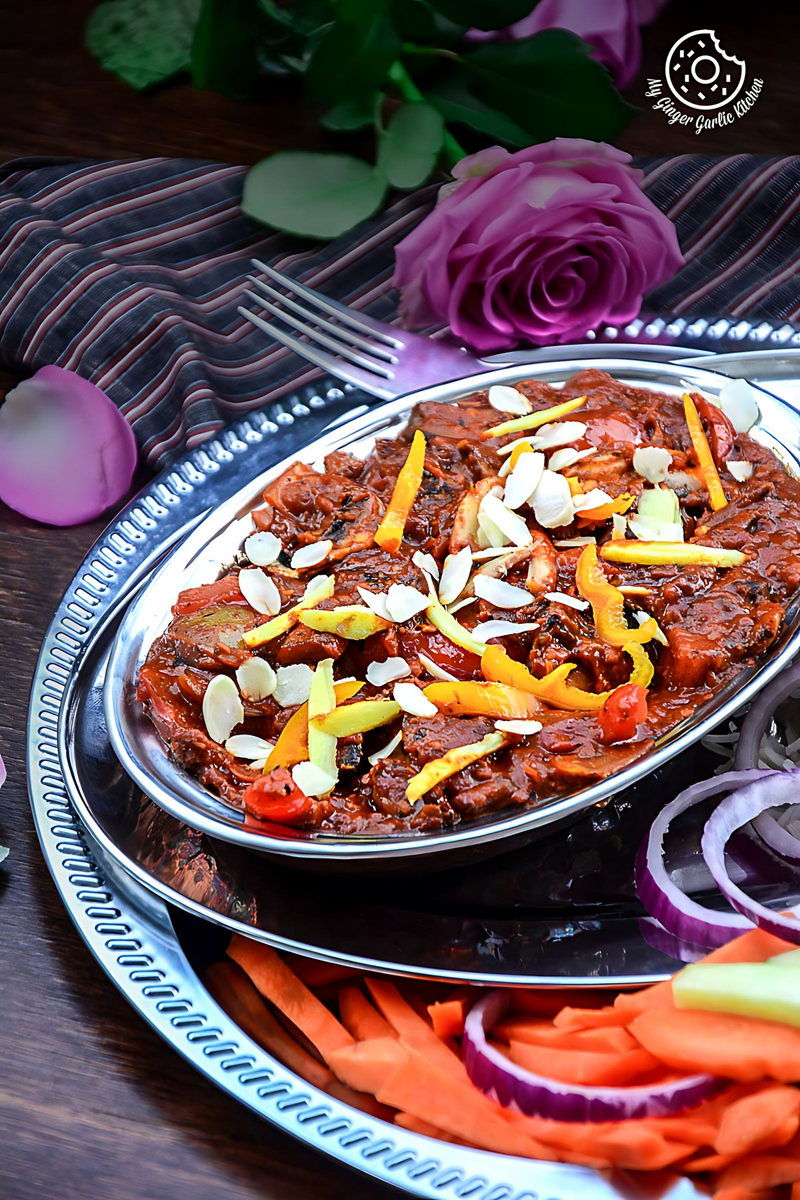 a plate of shahi kadai mushroom topped with almonds, with roses and salad on the table