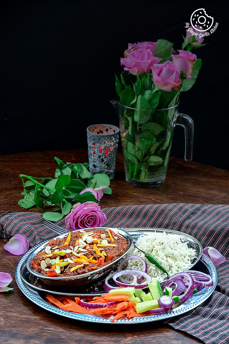 a plate of shahi kadai mushroom topped with almonds, rice, with roses and salad on a table with a vase of flowers