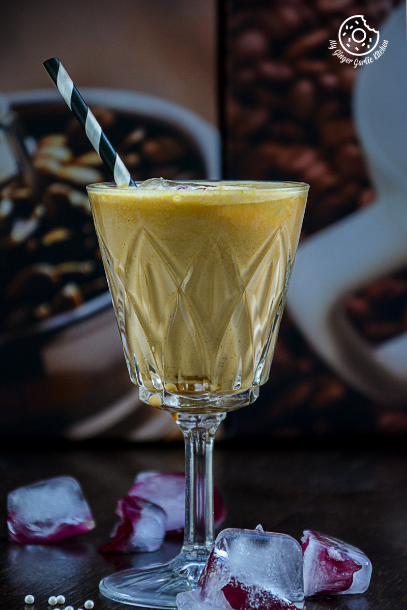a glass of a spiced chai pumpkin smoothie drink with a straw and ice cubes