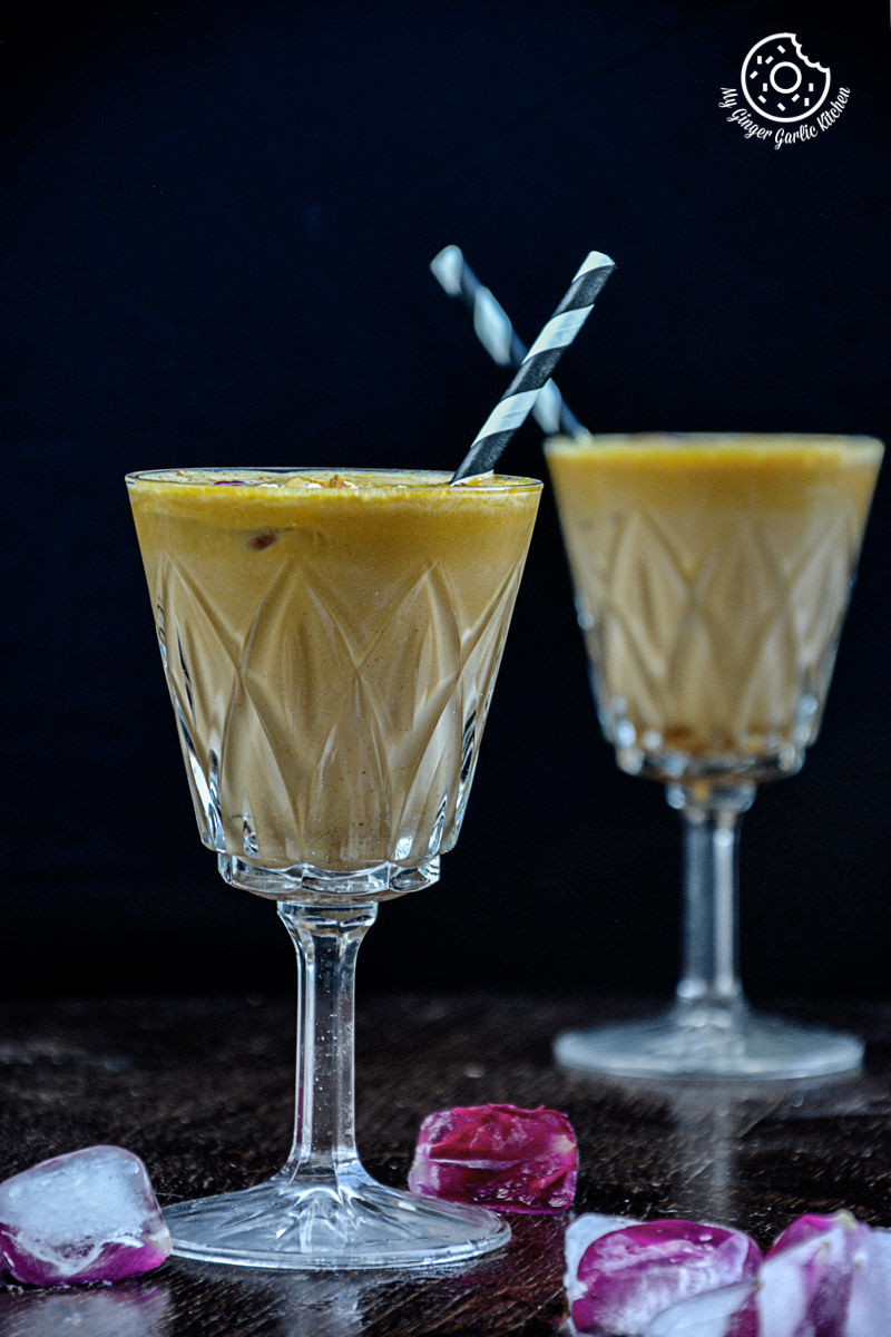 two glasses of spiced chai pumpkin smoothie with straws and ice cubes on a table