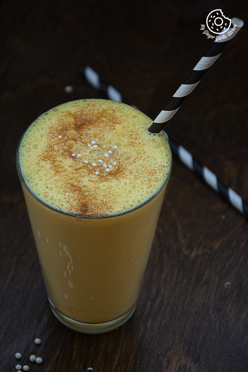 a glass of a spiced chai pumpkin smoothie drink with a straw and a striped straw