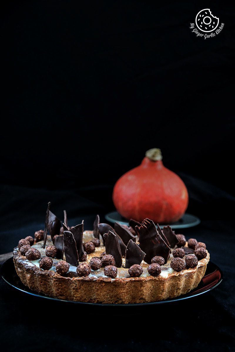 a spiced pumpkin pie with chocolate shaving and candies on it with a pumpkin in background