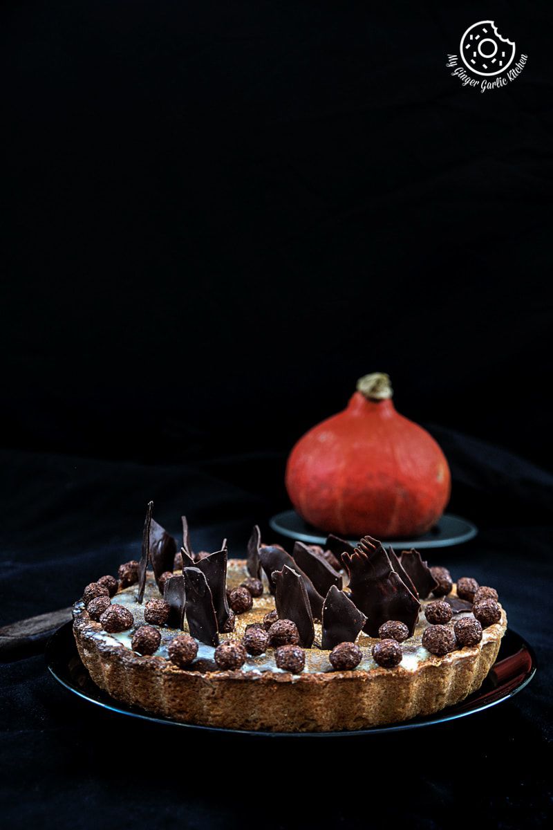 a spiced pumpkin pie with chocolate shaving and candies on it with a pumpkin in background