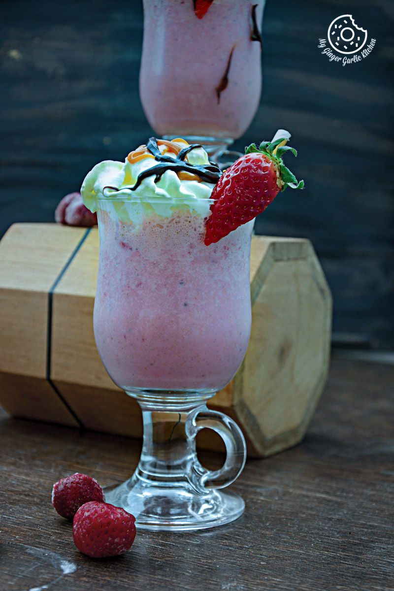 a glass of strawberry cake shake with a strawberries on top
