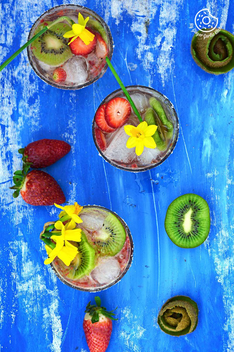 two glasses of strawberry kiwi sparkling cooler and floweres on a blue table