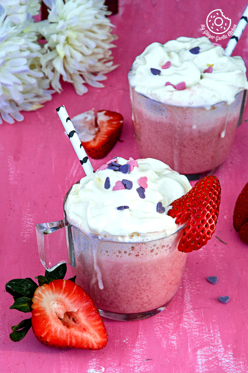 two cups of strawberry white hot chocolate with strawberries and a straw