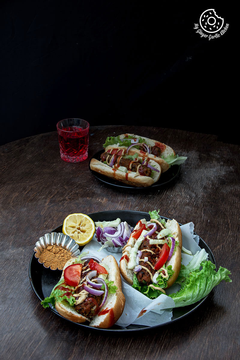 two sweet potato cabbage hot dogs on a plate on a table with a glass of juice