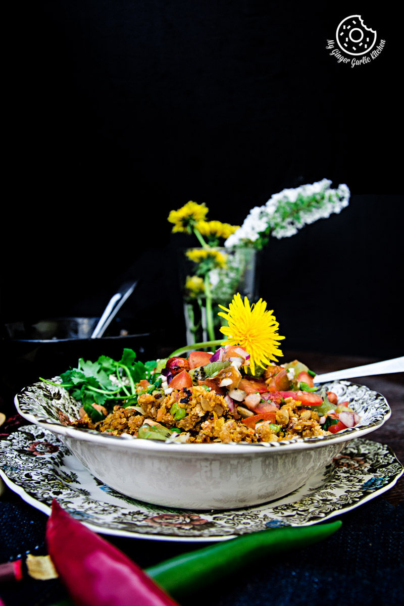a plate of tortilla poha topped with kiwi peanut salsa with a flower on top of it, with flower vas in background