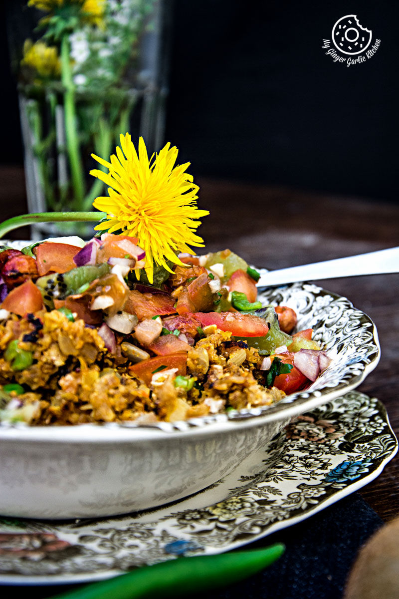 a plate of tortilla poha topped with kiwi peanut salsa with a flower on top of it, with flower vase in background