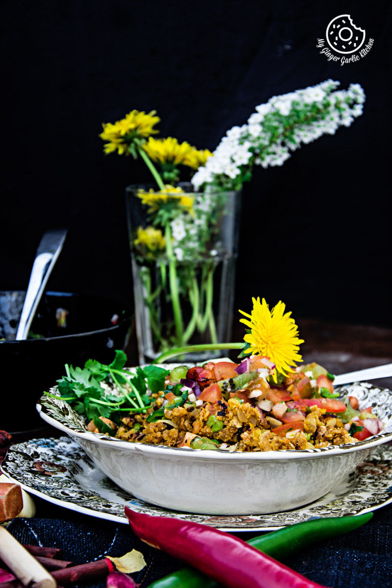 a plate of tortilla poha topped with kiwi peanut salsa with a flower on top of it, with flower vase in background