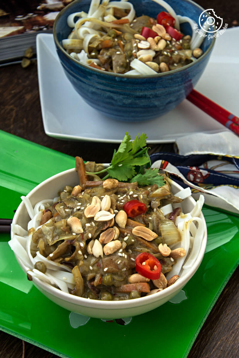 a bowl of vegan thai green curry vegetable noodles and peanuts on a green tray with a spoon