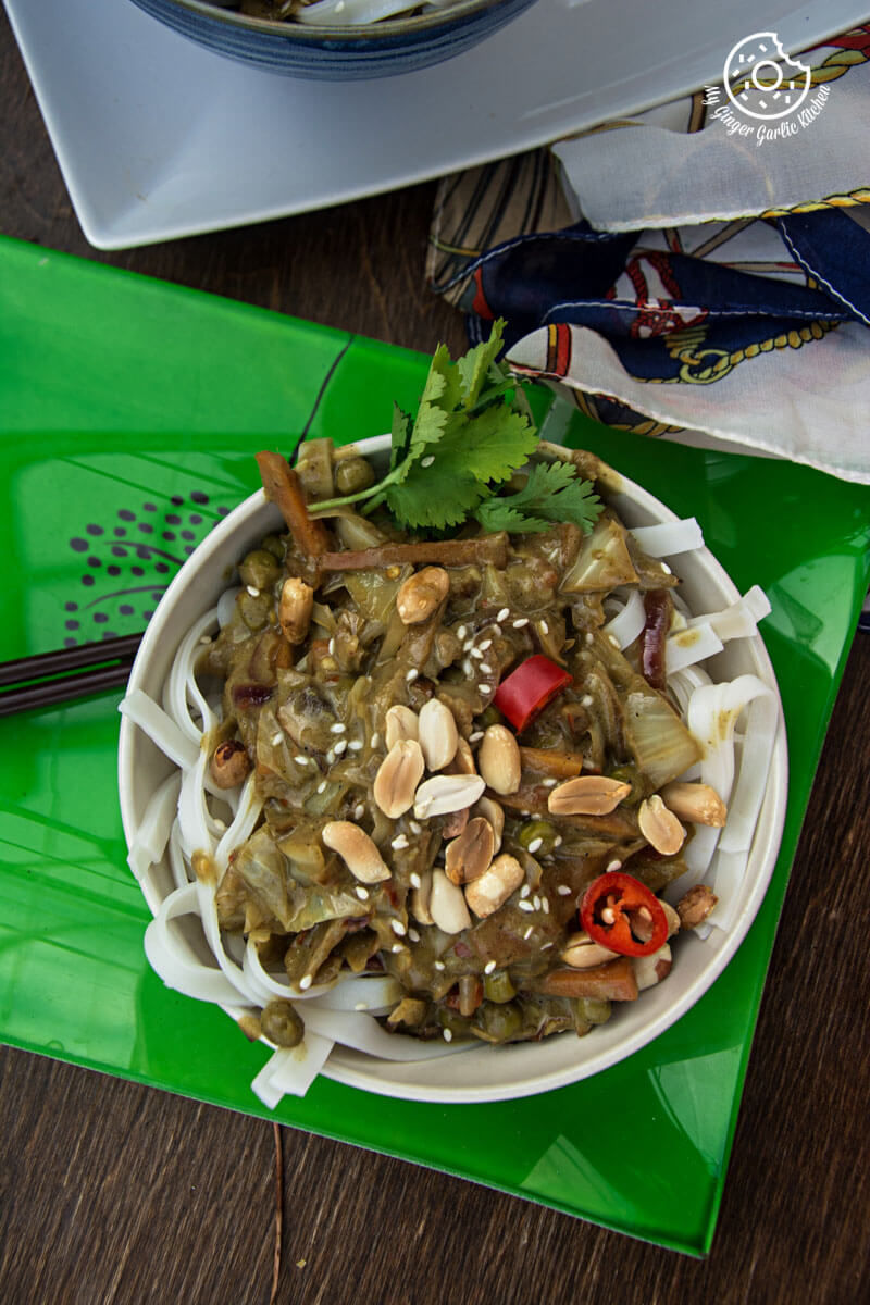 a bowl of vegan thai green curry vegetable noodles and peanuts on a green plate with a spoon