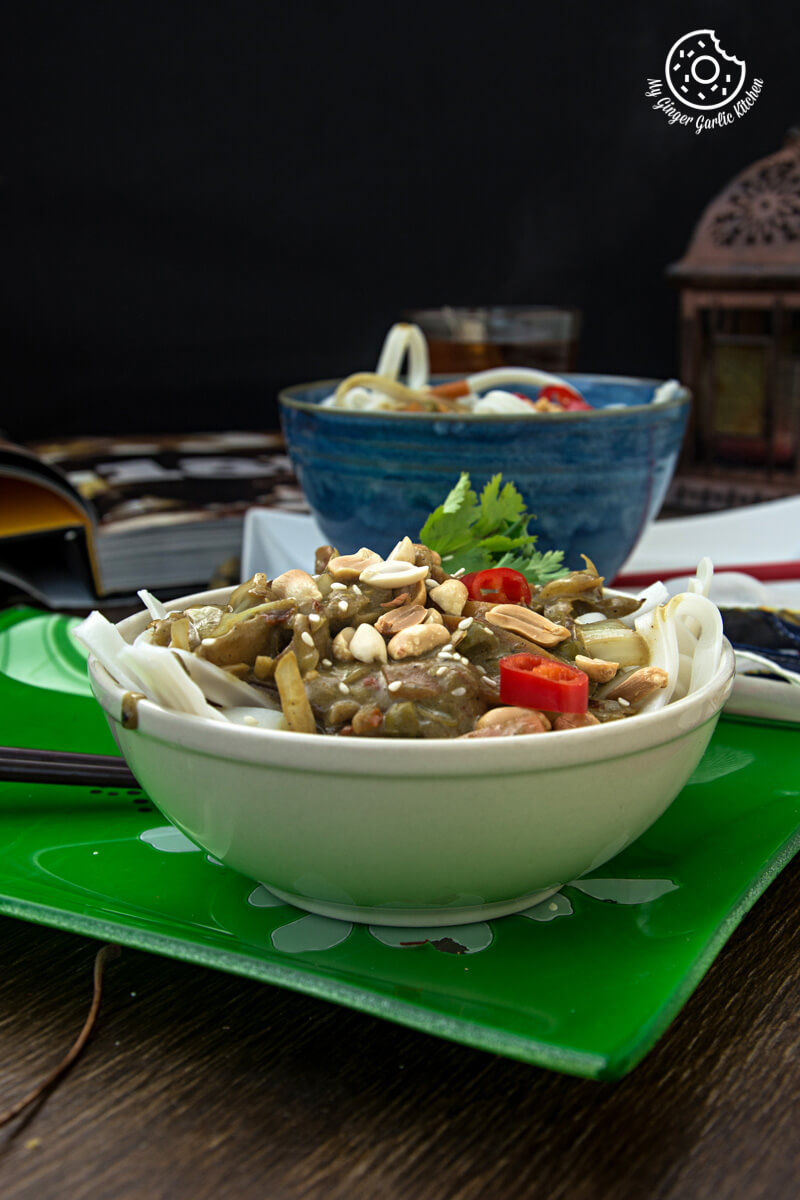 a bowl of vegan thai green curry vegetable noodles and peanuts on a green plate on a table