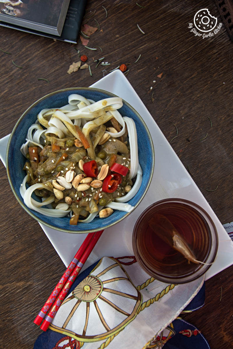 a bowl of vegan thai green curry vegetable noodles and chopsticks on a table