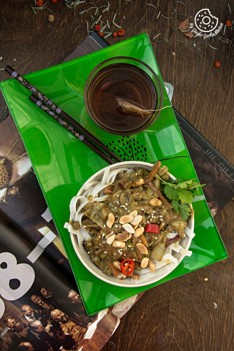 a bowl of vegan thai green curry vegetable noodles on a table with a magazine