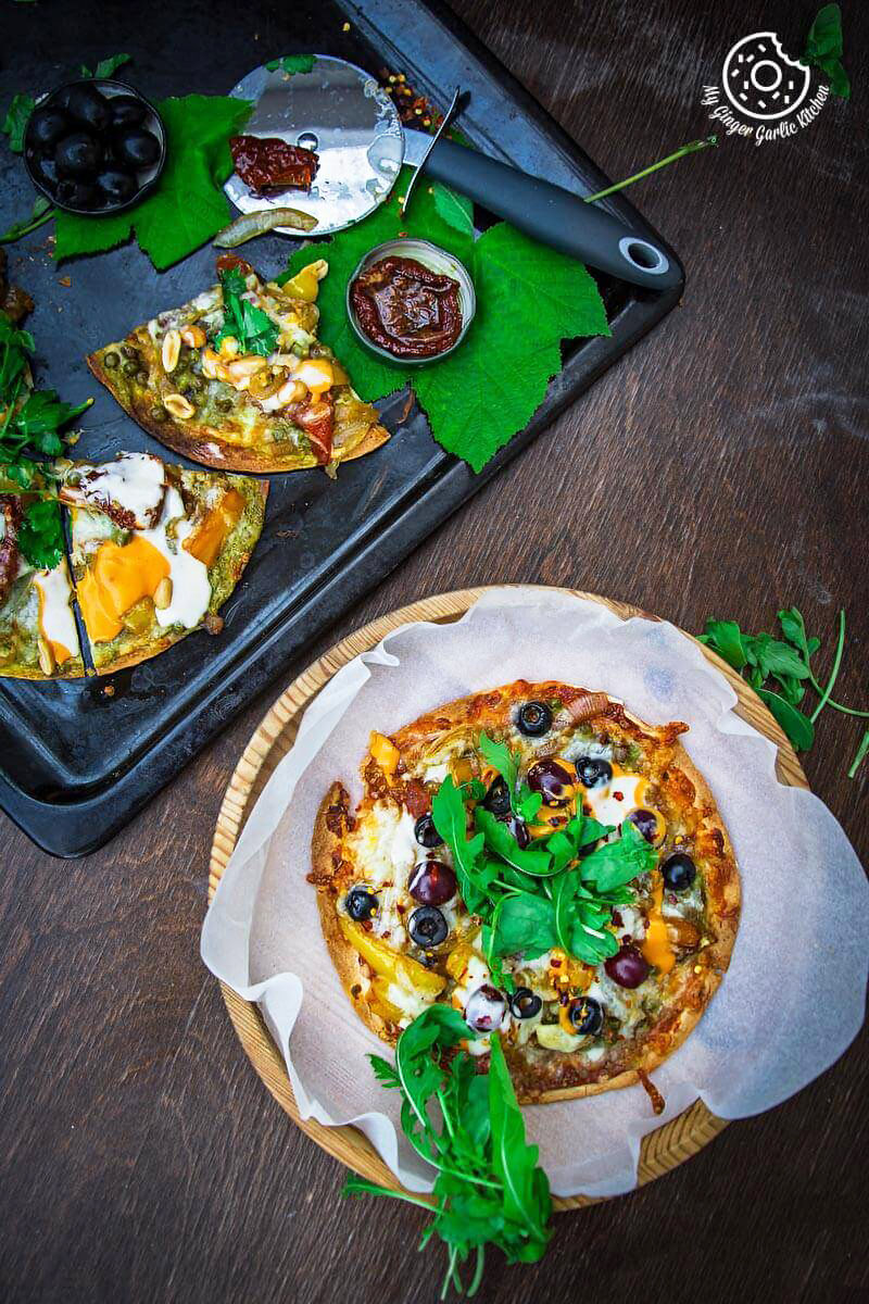 two a veggie tortizza or tortilla pizzas on a tray with a knife and a bowl of olives