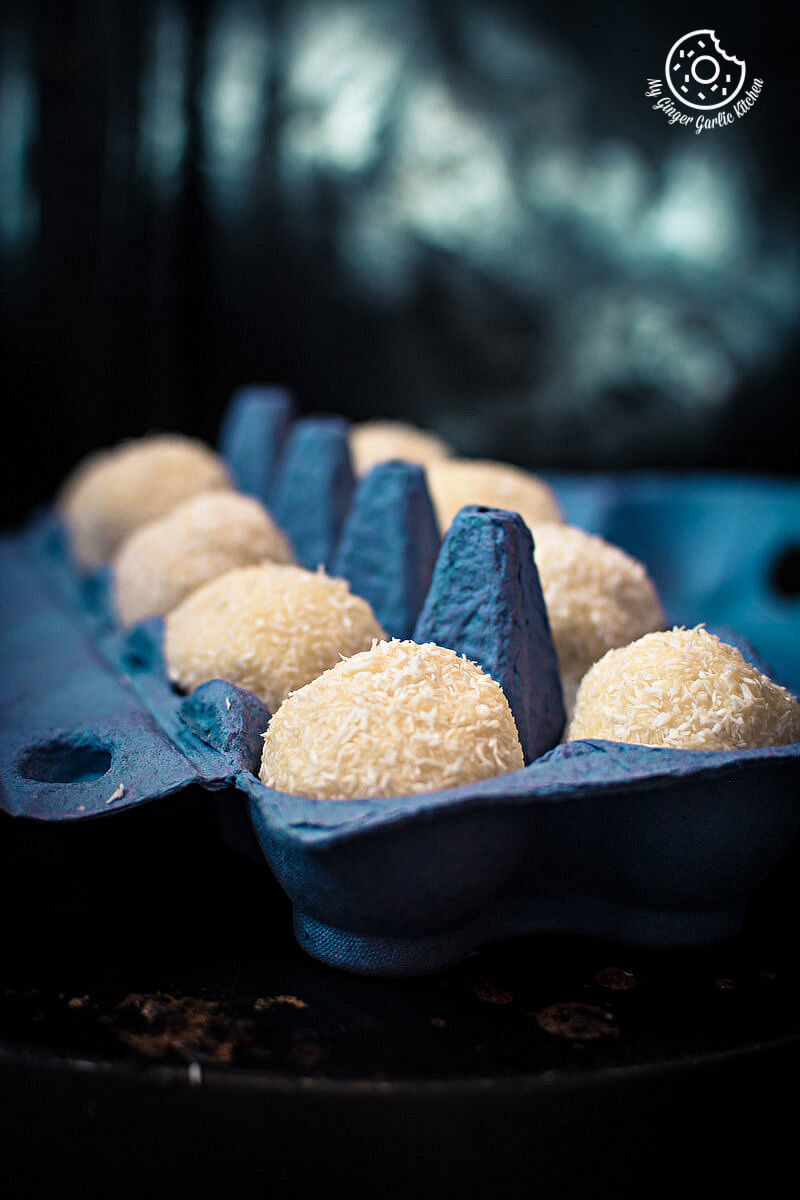 several bwhite chocolate coconut truffles in a blue egg carton on a table