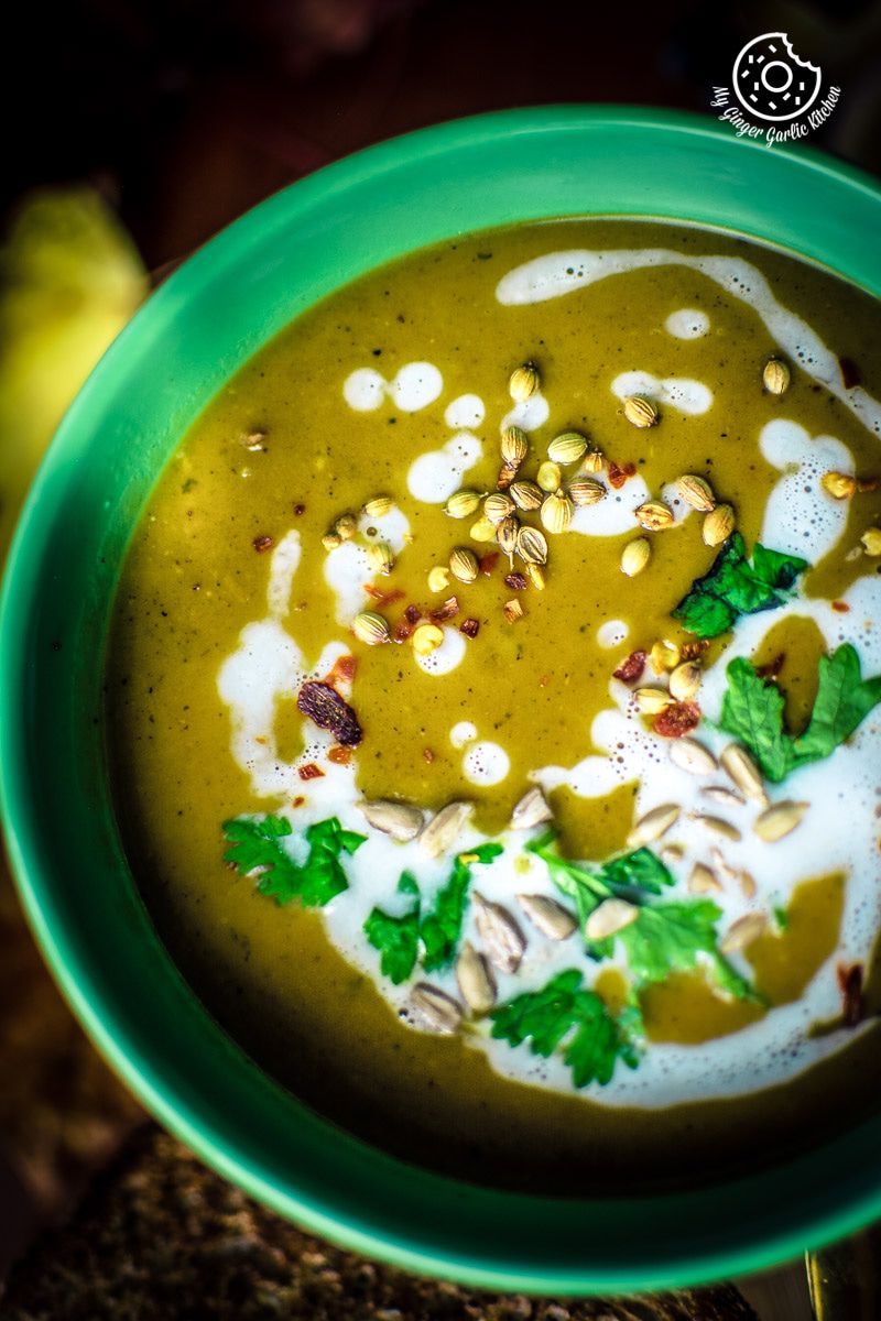 a green bowl of butternut squash soup with a spices and cream in it