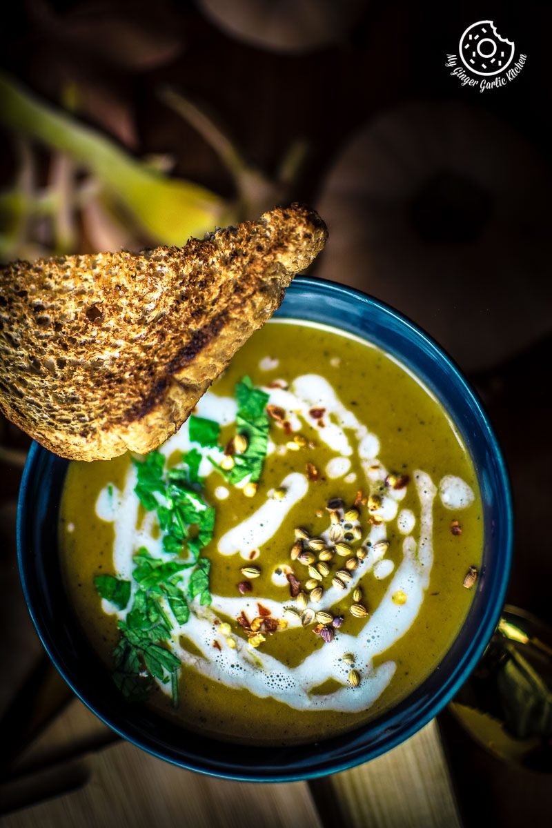 a bowl of butternut squash soup with cream and green garnish with a piece of toast