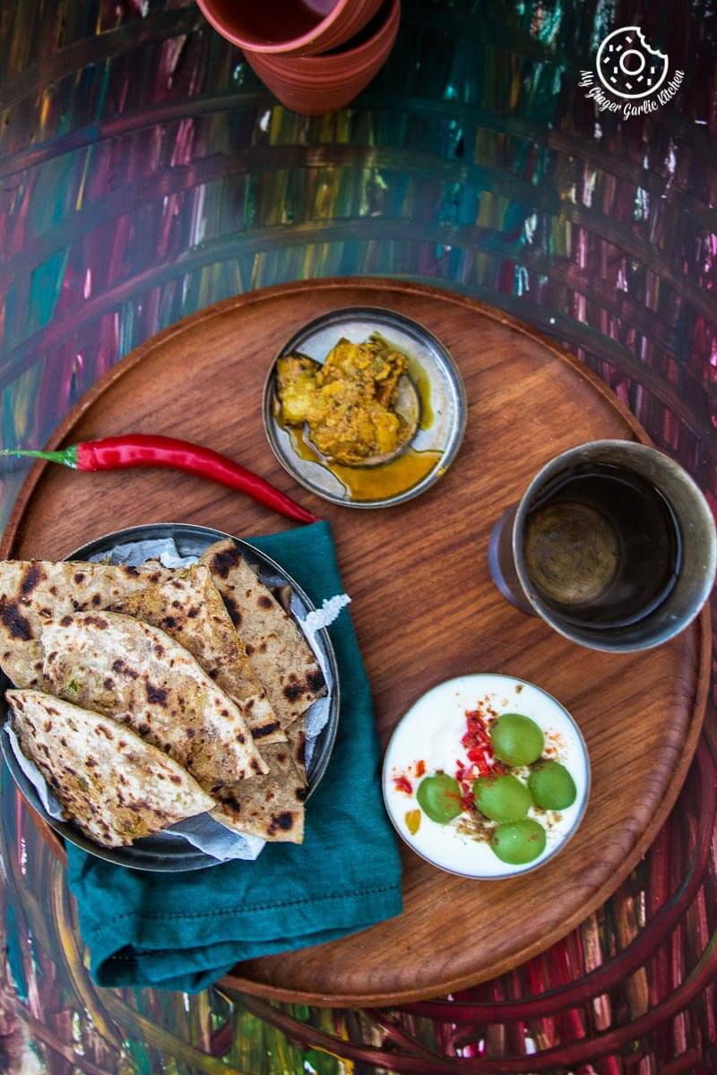 a plate of cabbage peas stuffed paratha on a table with a bowl of raita and a bowl pickle