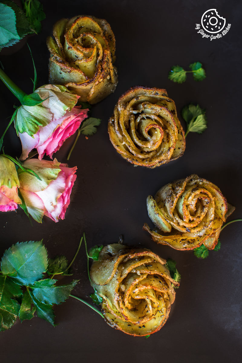 several potato roses or potato gratins  are arranged on a black surface with a few leaves
