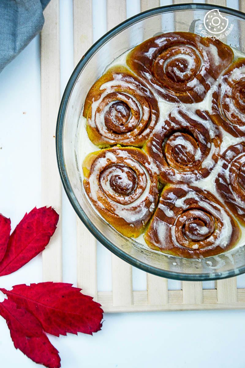 a glass dish with pumpkin cinnamon rolls on a wooden tray