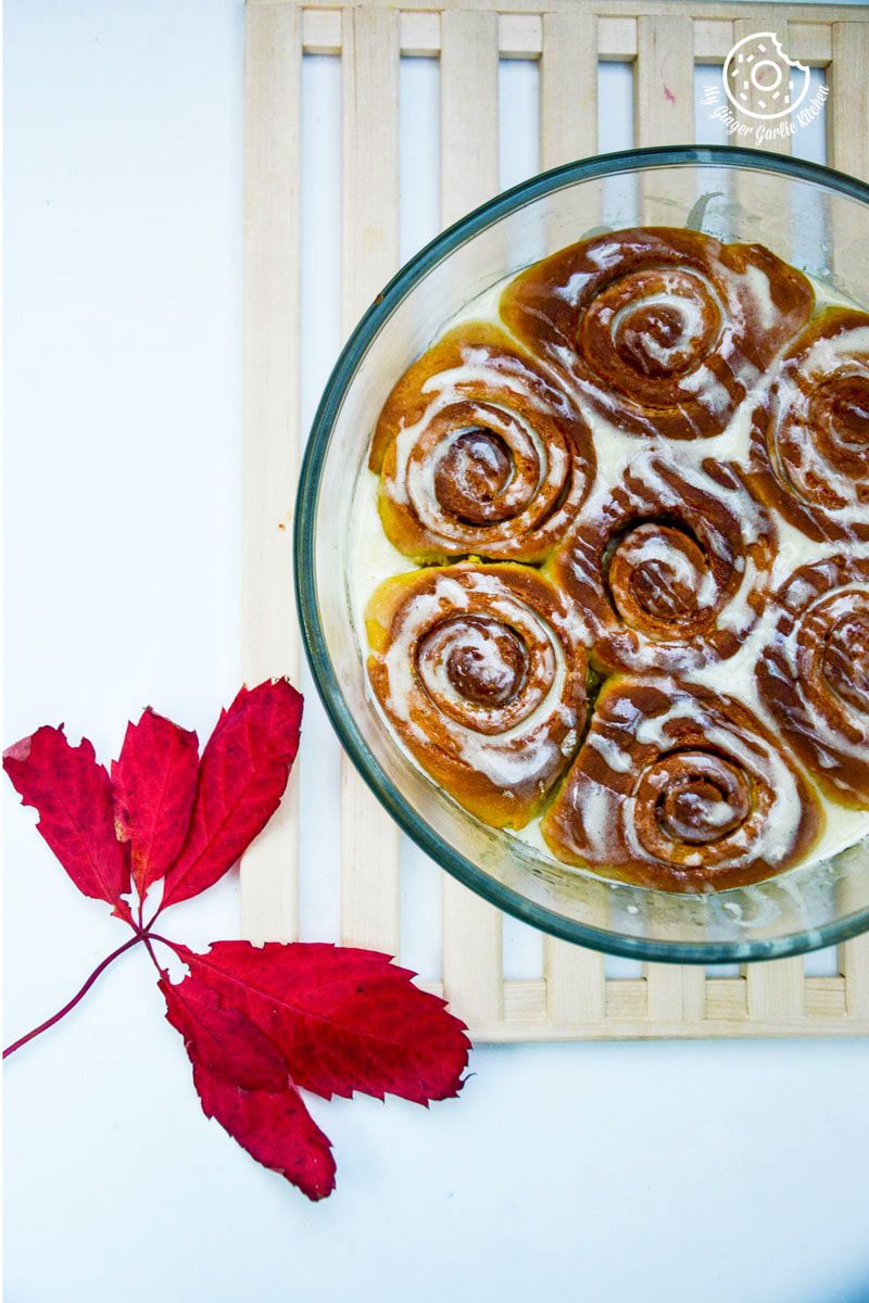 a glass bowl of pumpkin cinnamon rolls on a mat with a red leaf