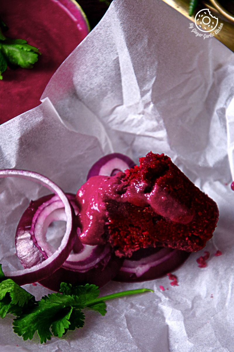 there is a roasted beet kebab dipped in a beet sauce with onions slices and a sprig of parsley