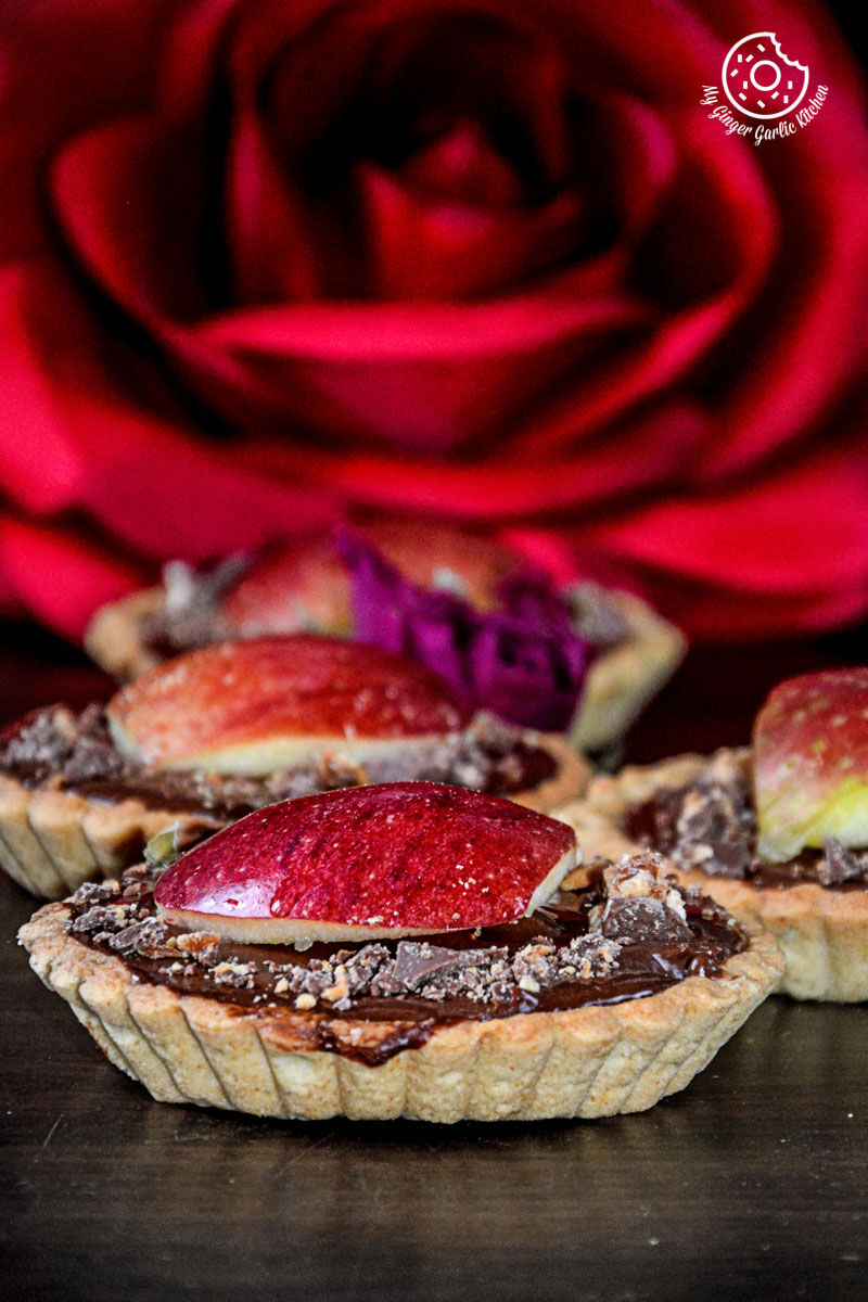 three snickers chocolate mini tart with chocolate and heart shaped apples on them