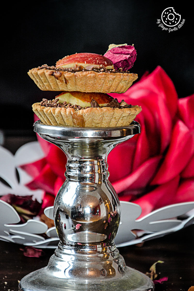 two snickers chocolate mini tarts on a silver plate with a rose in the background