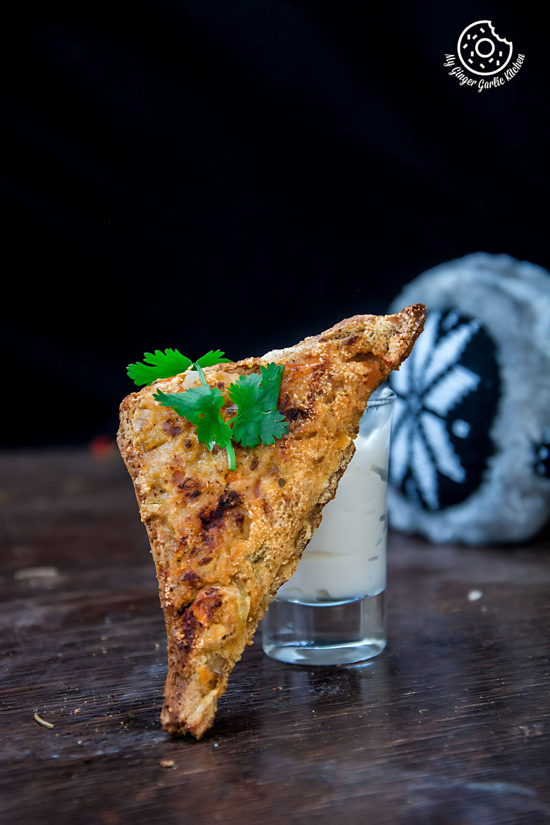 a slice of sooji toast rava toast with sprig of parsley on a table with a glass of sauce