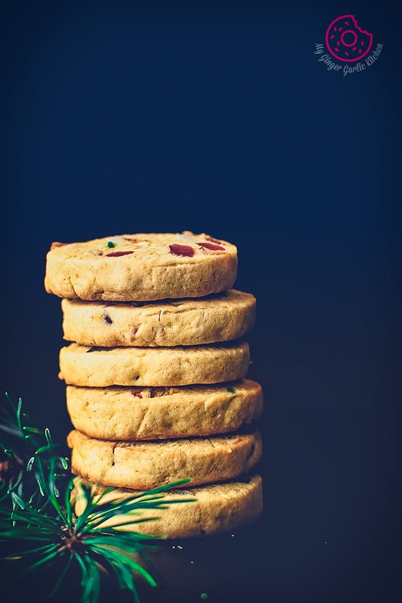 a close up of a stack of tutti frutti cookies with a sprig of rosemary