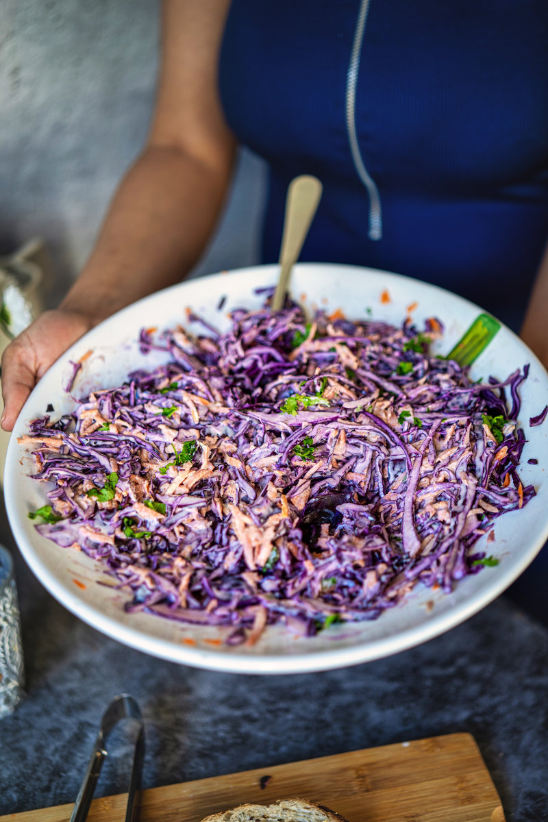 Hands holding a white plate filled with vibrant purple coleslaw made from shredded red cabbage, mixed with herbs and a creamy dressing. 