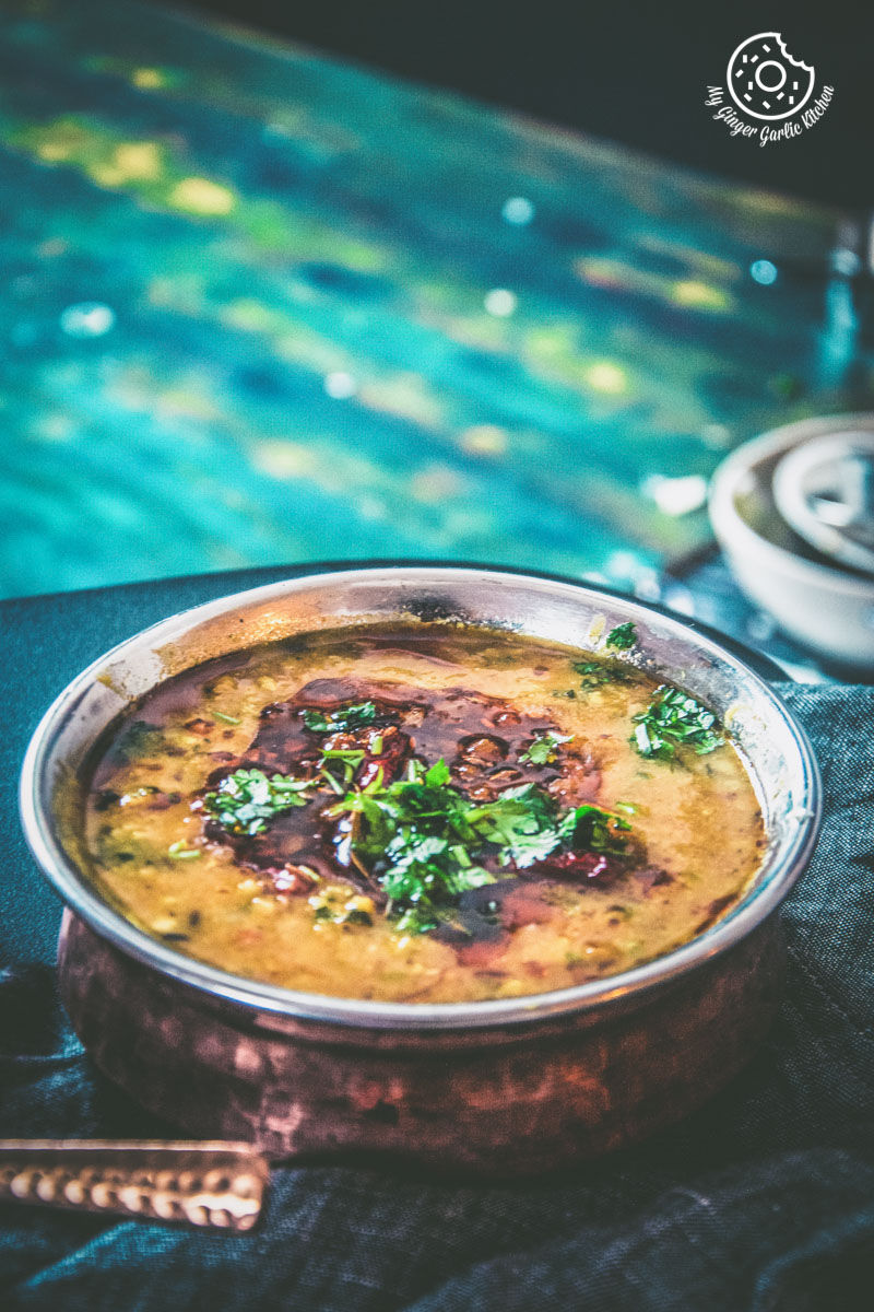 bowl of restaurant style dal tadka topped with tempering and cilantro kept on a wooden board