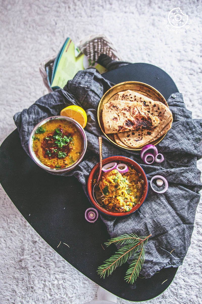 a bowl of restaurant style dal tadka with a bowl of dal rice and a plat of parathas on a table with a cloth