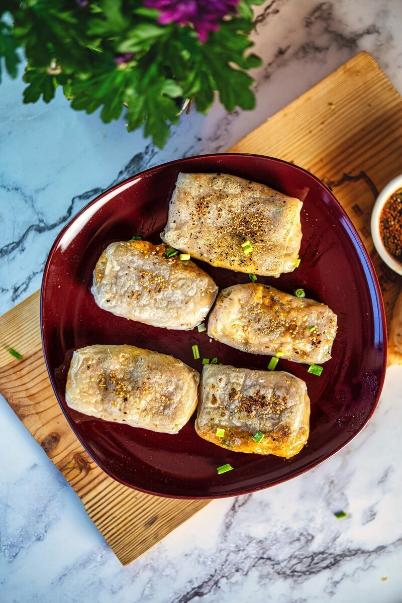 Crispy rice paper dumplings served on a red plate, sprinkled with green onions, perfect for Asian appetizer or vegan snack recipes