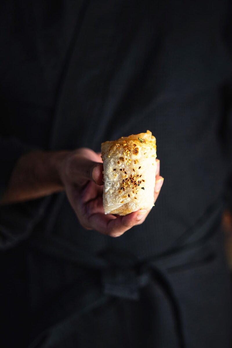 Person holding a homemade rice paper dumpling topped with sesame seeds, healthy vegan snack option