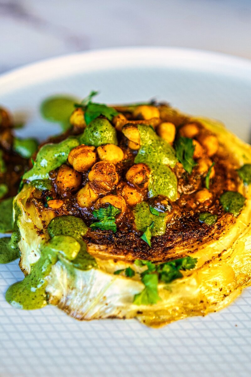 Crispy cabbage steak topped with spiced chickpeas and green tahini sauce on a serving plate