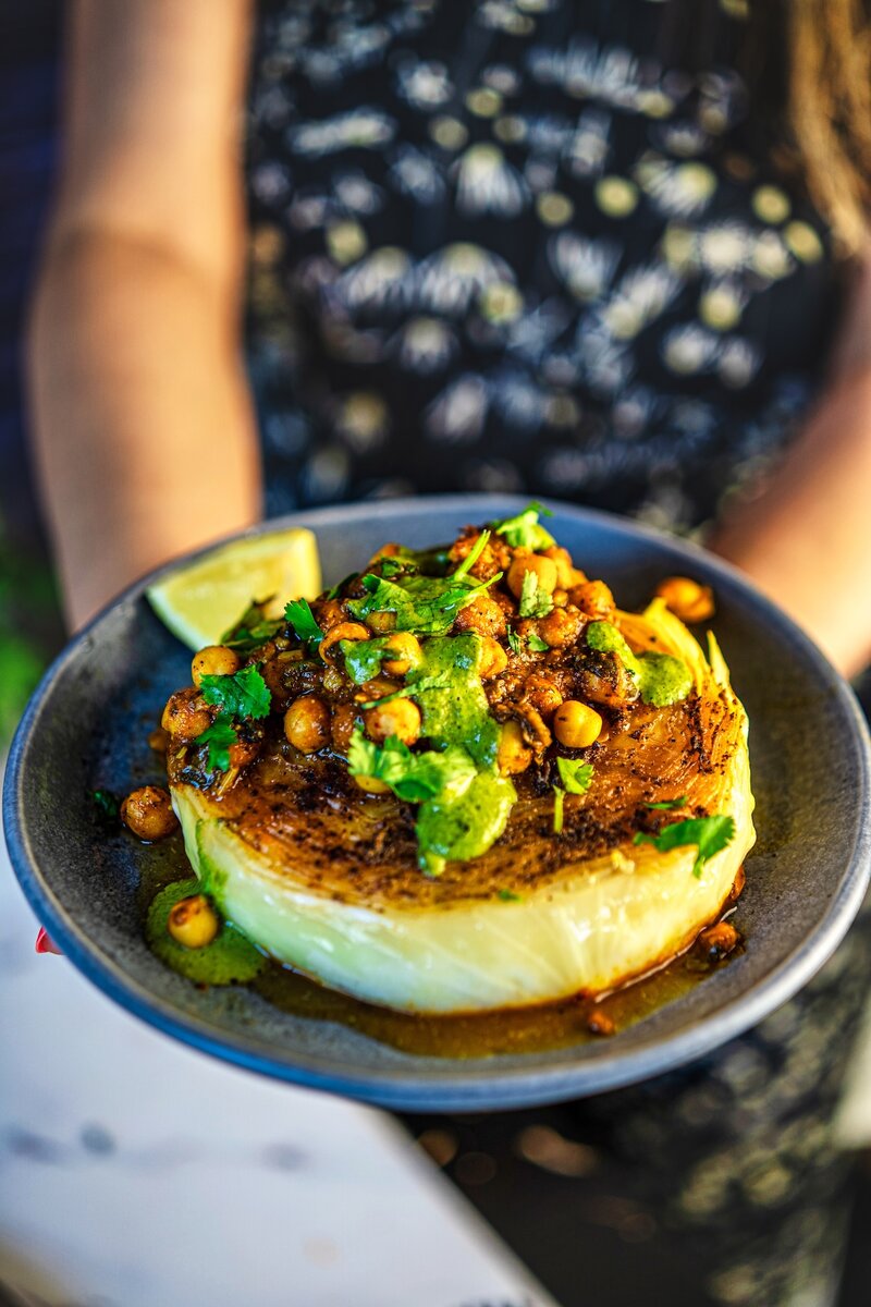 Golden roasted cabbage steak with chickpea topping and cilantro tahini sauce in natural light