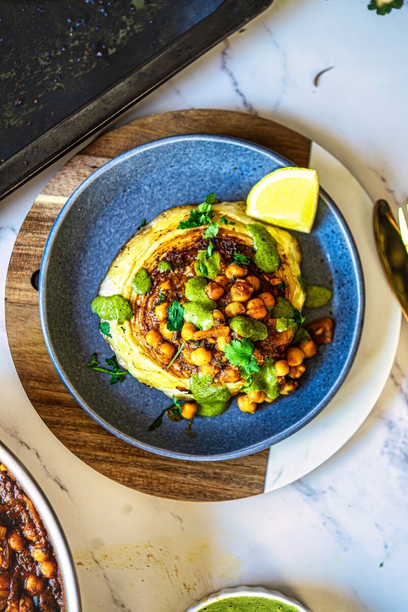 Top view of crispy roasted cabbage steaks with chickpea stew and cilantro tahini sauce on a plate