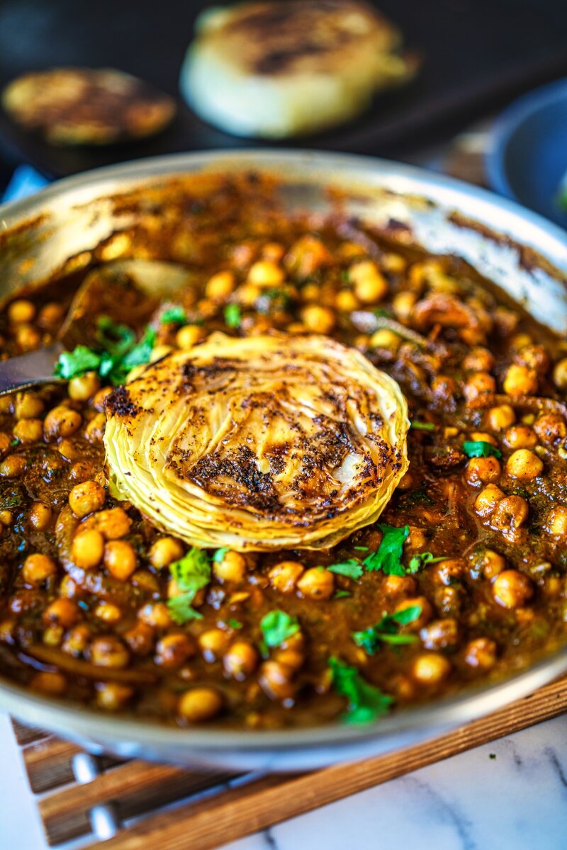 Close-up of roasted cabbage steak served over rich chickpea stew with herbs and spices