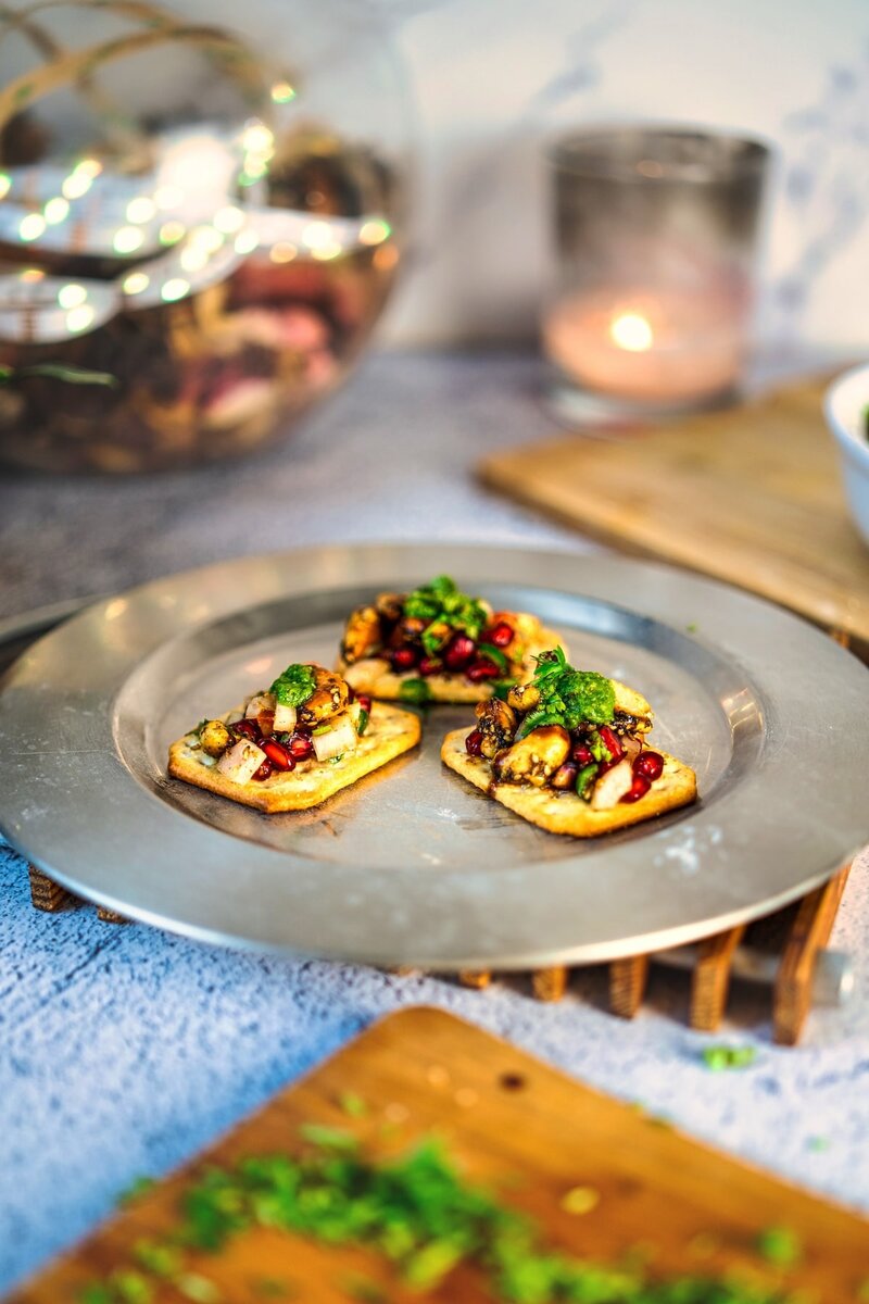 Hand holding a Sweet and Spicy Roasted Cashew Chaat Bite topped with chutney and pomegranate seeds