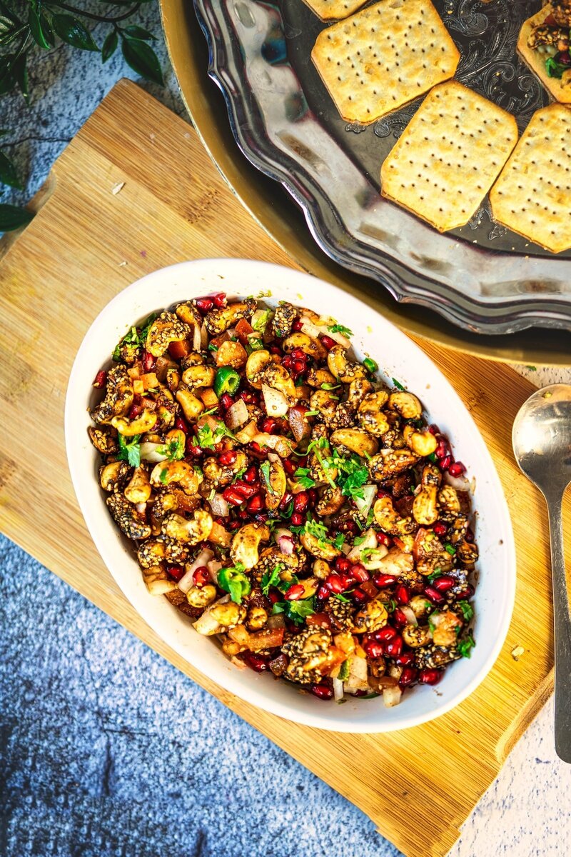 Sweet and Spicy Roasted Cashews Chaat Bites served on crackers with pomegranate, chutney, and herbs on a festive plate