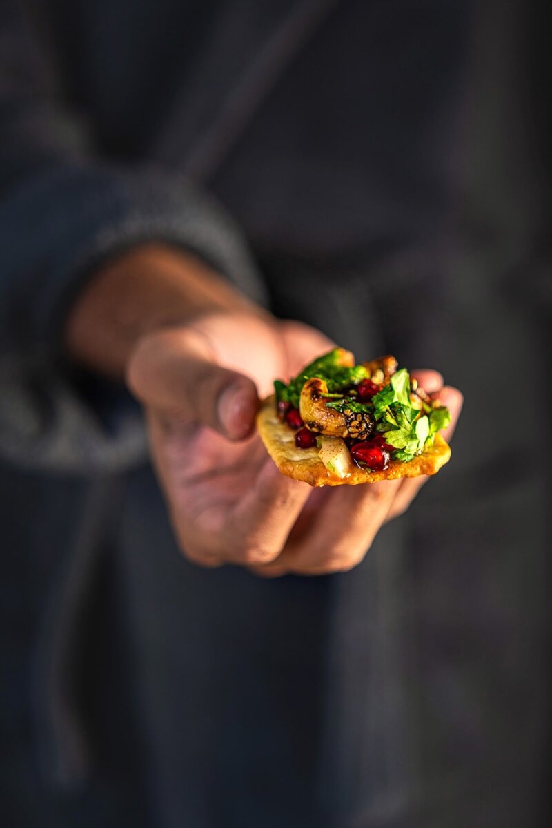 Close-up of Sweet and Spicy Roasted Cashew Chaat Bite topped with mint chutney, pomegranate, and sesame seeds on a cracker