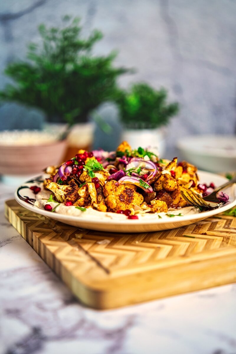 Side view of a Roasted Cauliflower Tahini Bowl with roasted cauliflower and potatoes, creamy tahini yogurt, almonds, and fresh herbs