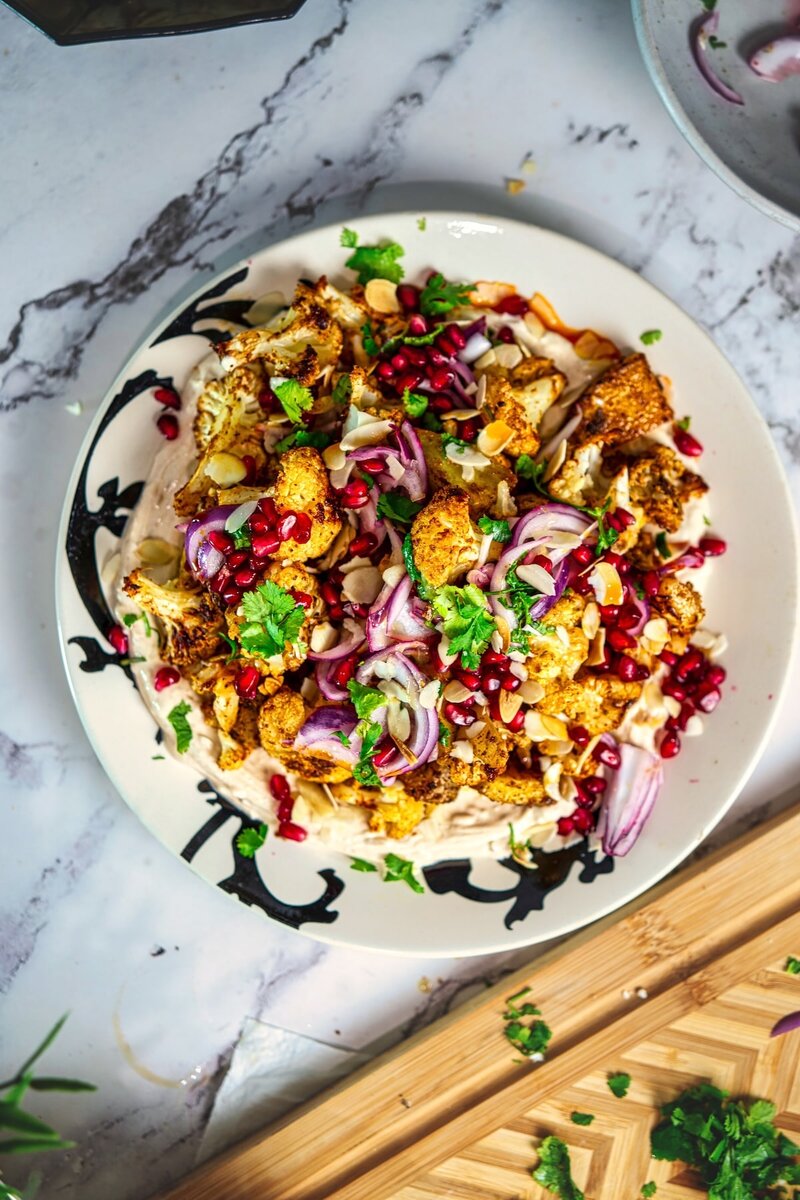 Roasted Cauliflower Tahini Bowl topped with crispy roasted cauliflower, potatoes, onion salad, pomegranate arils, almonds, and chili oil