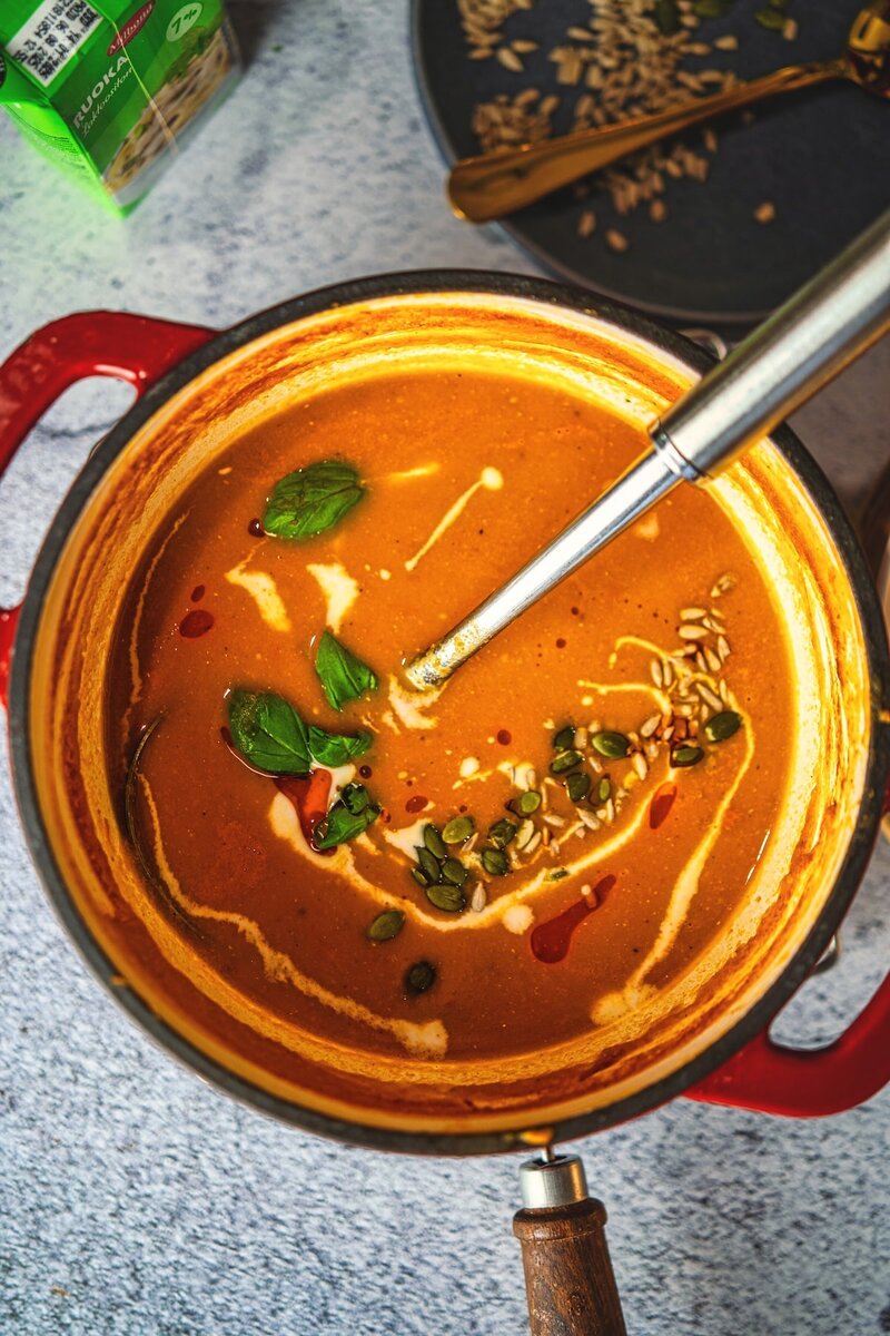 Creamy roasted tomato basil soup simmering in a pot with coconut cream, basil leaves, and pumpkin seeds.
