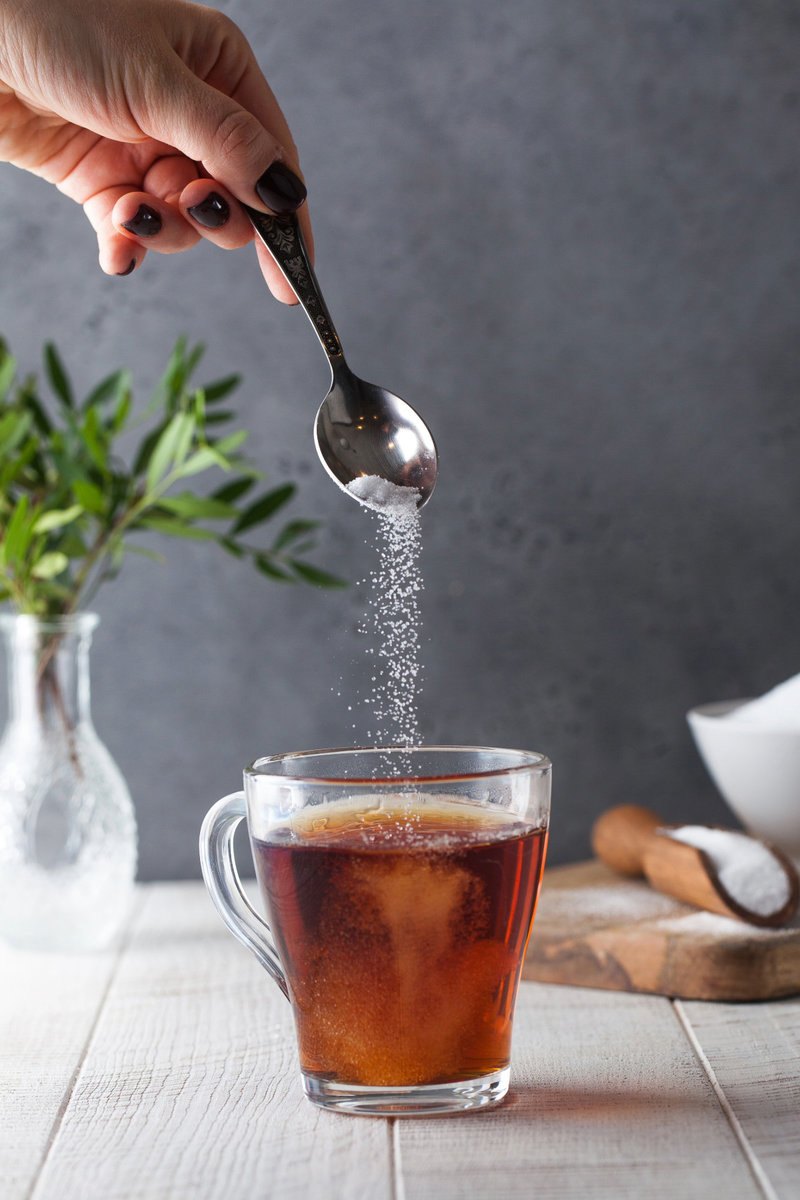Woman adding sugar to a cup of tea, demonstrating the typical use of sweeteners which could be substituted with stevia during intermittent fasting.