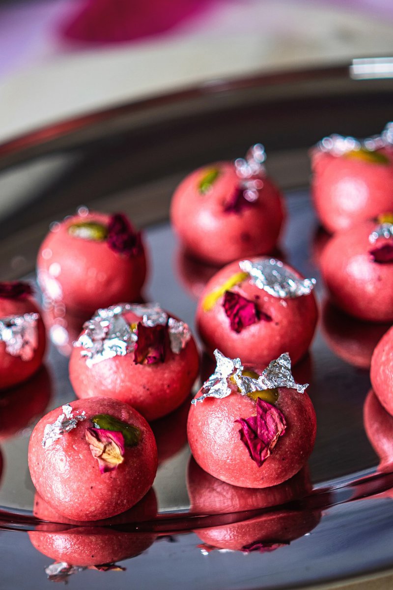 Close-up of pink rose badam ladoos garnished with edible silver and rose petals on a shiny plate.