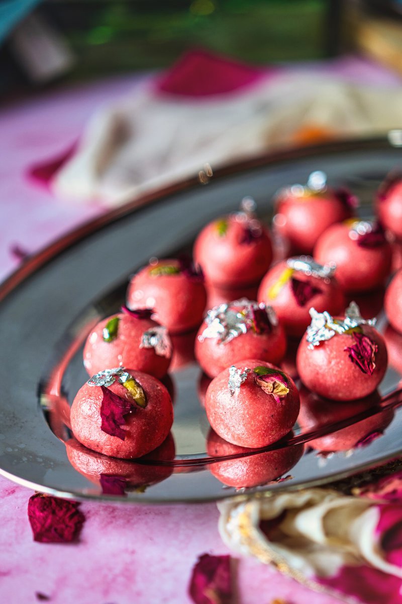 No Cook Rose badam ladoos or Almond Ladoos decorated with dried rose petals and silver foil on a reflective plate.